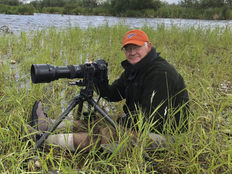 Photographer sitting in grass with camera equipment.