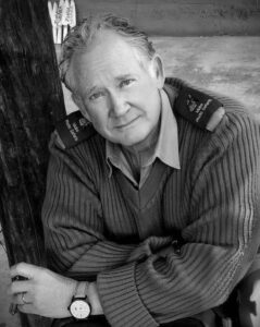 Man in sweater sitting outdoors, black-and-white.